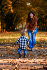 A little boy in a shirt and jeans runs to mom against the backdrop of an autumn park, view from back. Mom and son.