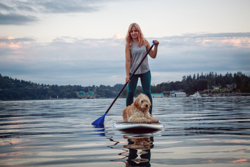 Girl with a dog on a paddle board during a vibrant summer sunset. Taken in Deep Cove, North...