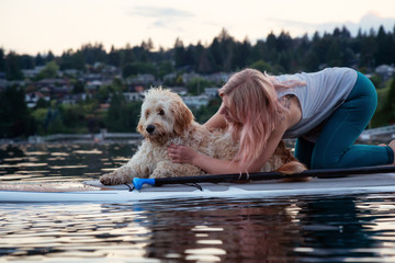 Girl with a dog on a paddle board during a vibrant summer sunset. Taken in Deep Cove, North Vancouver, BC, Canada.