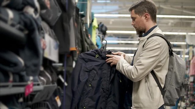Grown man choosing new sport jacket for daily wear. Man holding nice black coat and checking quality, brand and price. Sport style.