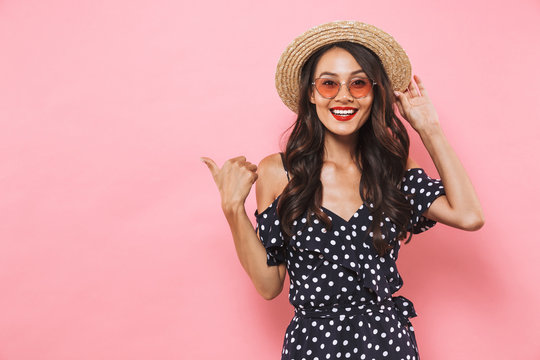 Happy brunette woman in straw hat and sunglasses pointing away