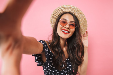Happy brunette woman in straw hat and sunglasses making selfie