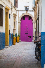 The old, lined wooden door is lilac in the background of the plastered peeling wall. Moroccan style. Africa, Morocco, Essaouira