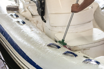 Man washing white inflatable boat with brush and pressure water system at garage. Ship service and...