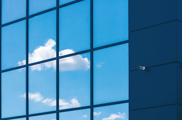 Glass facade of modern office building with security camera and reflected clouds