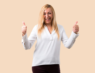 Middle age blonde woman with white shirt giving a thumbs up gesture with both hands and smiling....