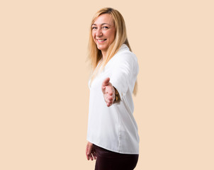 Middle age blonde woman with white shirt handshaking after good deal on isolated ocher background