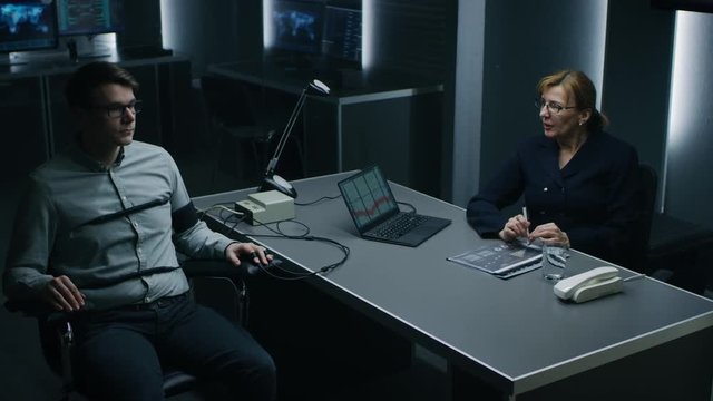 Female Special Agent Conducts Lie Detector / Polygraph Test on a Young Suspect. Expert Examiner Questions Accused in Interrogation Room. Laptop Records Reactions.