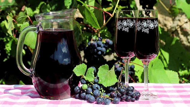 Wineglass with full carafe and a ripe grapes on a table, a vineyard on background. Two full wine glass of red wine with grapes on vineyard.
