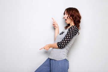 happy young woman pointing fingers at copy space on gray wall