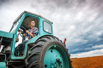 Photo sur Plexiglas Tracteur Young beautiful girl working on a tractor in the field, unusual work for women, gender equality concept