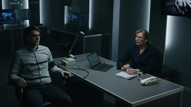 Female Special Agent Conducts Lie Detector / Polygraph Test on a Young Suspect. Expert Examiner Asks Accused Yes or No Questions in Interrogation Room. Computer Records Reactions.