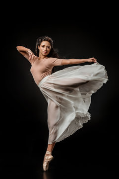 young female ballet dancer in white skirt posing on dark backdrop