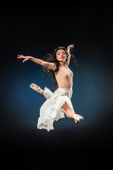 Fototapeta na wymiar young ballerina in elegant clothing jumping on dark backdrop