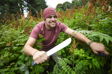 A man with a machete making his way through a thicket, sailor pirate in the jungle