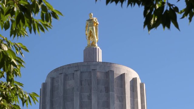 The gold Oregon Pioneer Man statue on top of the Oregon State Capitol building Rotunda in Salem, tree branches in the edges of the frame.