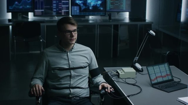 Young Handsome Suspect During Interrogation Undergoes Lie Detector / Polygraph Test, Connected to the Machine He Answers Yer or No Questions Which Computer Records and Shows if He's Lying.