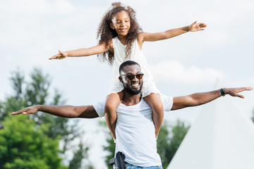 african american police officer with gun holding daughter on shoulders and they pretending flying...