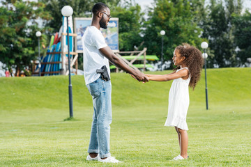 african american policeman with gun and daughter holding hands and spinning around in amusement park