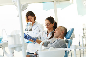 Dentist and his assistant in dental office talking with female patient and preparing for...