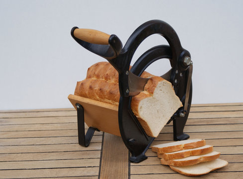 Alte d&auml;nische Brotschneidemaschine auf h&ouml;lzernem Untergrund mit Wei&szlig;brotscheiben