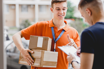 A smiling person wearing an orange T-shirt and a name tag is delivering a parcel to a client, who...