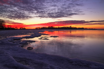 Fototapeta na wymiar Beautiful colorful winter landscape with frozen lake and sunset sky. Unusual weather phenomenon
