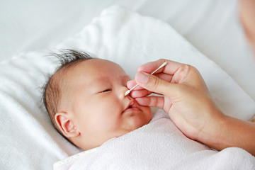 Close-up mother use cotton bud to clean baby nose.
