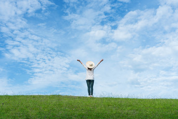 Standing woman raised her hands on the mountain, natural green and beautiful sky.