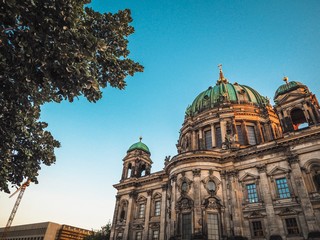 Obraz premium The dome of the berlin cathedral against the blue sky and green tree branches