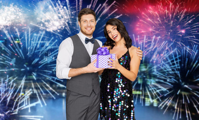 holidays, celebration and people concept - happy couple with gift box at party over firework background