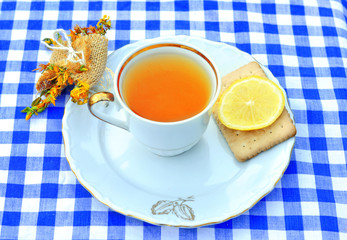 Cup of hot tea with lemon slice.Rustic white porcelain cup a herb wrapped up as a gift on a  blue- white checkered tablecloth. Top view. Healthy concept. Copy space
