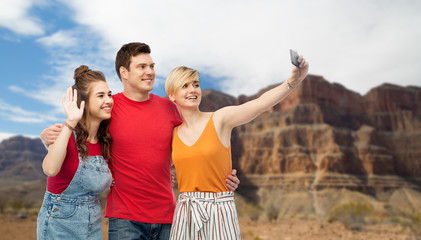 travel, tourism and summer holidays concept - group of happy smiling friends taking selfie by smartphone over grand canyon national park background