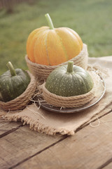 One orange pumpkin and two green pumpkin on the wooden table decorated burlap and rope. Outdoors.