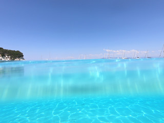 Underwater photo of tropical paradise turquoise exotic beach of Voutoumi with sail boats docked in island of Antipaxos, Ionian, Greece