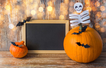 holidays, school and party concept - halloween pumpkins, decorations with blank chalkboard on wooden boards background