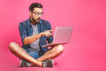 Wow! Online working concept. Casual business man relaxed working and browsing internet on laptop computer. Freelance sitting and typing on laptop keyboard at home office. Pink background.