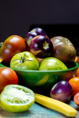 Multicolored assortment of French fresh ripe tomatoes in green bowl on blue wooden table, dark key