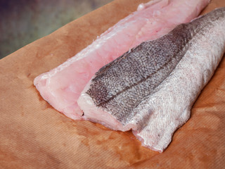 Two raw fillets of hake, fish, on brown paper
