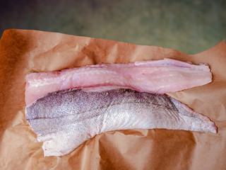 Two raw fillets of hake, fish, on brown paper
