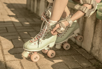 Skater girl putting on mint retro roller skates outdoor