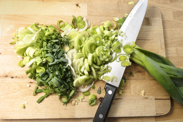 sliced leek and a large kitchen knife on a wooden board, cooking concept, high angle view from above