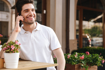 Cheerful man sitting in cafe outdoors while talking by mobile phone.