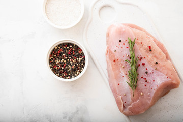 Raw turkey breast fillets on wooden cutting board with herbs, spices over white table. top view...