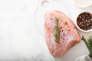 Raw turkey breast fillets on wooden cutting board with herbs, spices over white table. top view with copy space