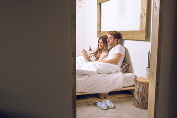 Couple of guy and girl lying in bed watching the cell phone