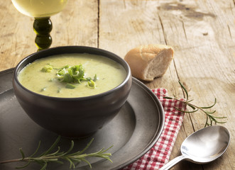 leek cream soup in a dark bowl on a plate, wine, bread and spoon on a rustic wooden table, copy space