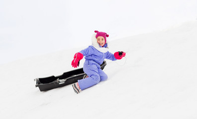 Fototapeta na wymiar childhood, sledging and winter season concept - happy little girl with sled on snow hill