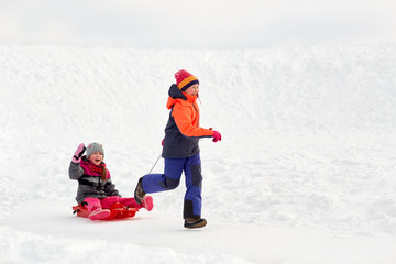 childhood, leisure and season concept - happy little girls in winter clothes with sled having fun outdoors