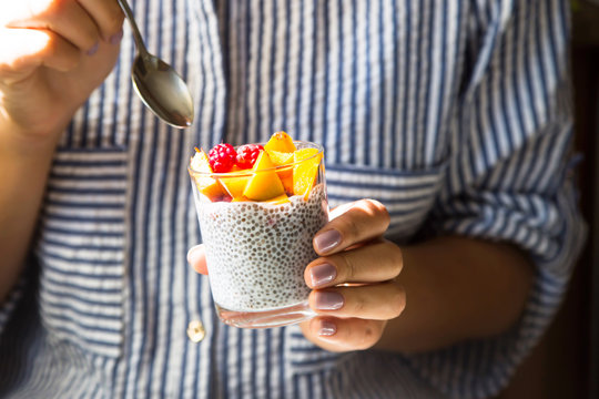 Chia pudding on coconut milk with raspberries and peach in a glass jar in female hands with a spoon. Raw vegan healthy food concept